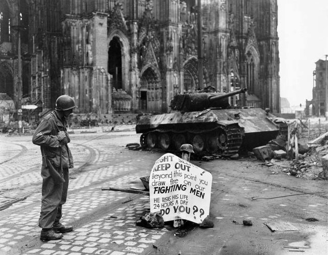 24.) Corporal Luther E. Boger of US 82nd Airborne Division reading a warning sign, Cologne, Germany (April 4, 1945).