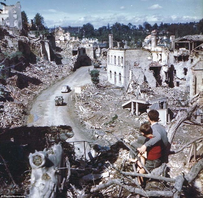 18.) In the aftermath of the D-Day invasion, two boys watch from a hilltop as American soldiers drive through the town of St. Lo. France (1944).