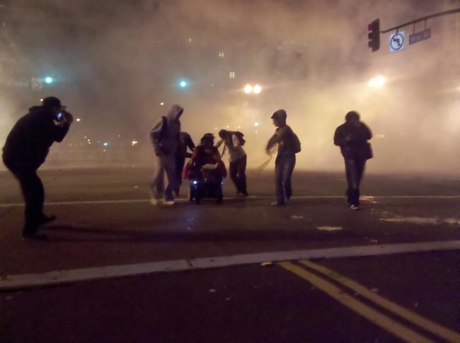 4.) Protestors in Oakland, California, help a woman in a wheelchair get away from teargas.