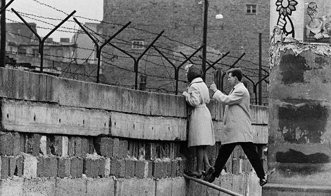 A couple in West Berlin peers over the Berlin Wall as the woman speaks to her mother on the other side.