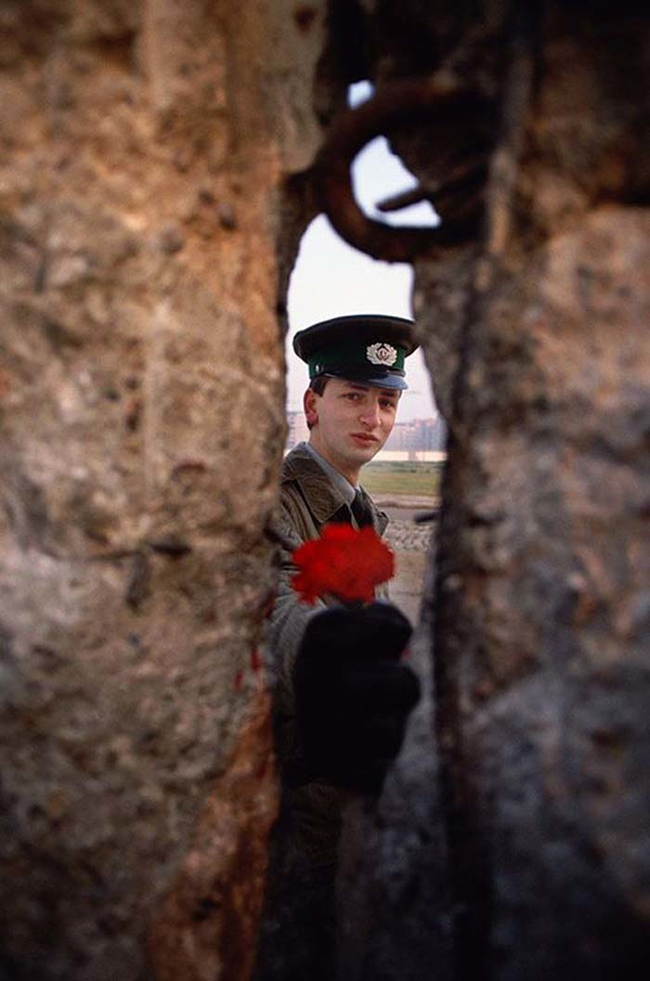 18.) 1989 - East German soldier passing a flower through the Berlin Wall before it was torn down.