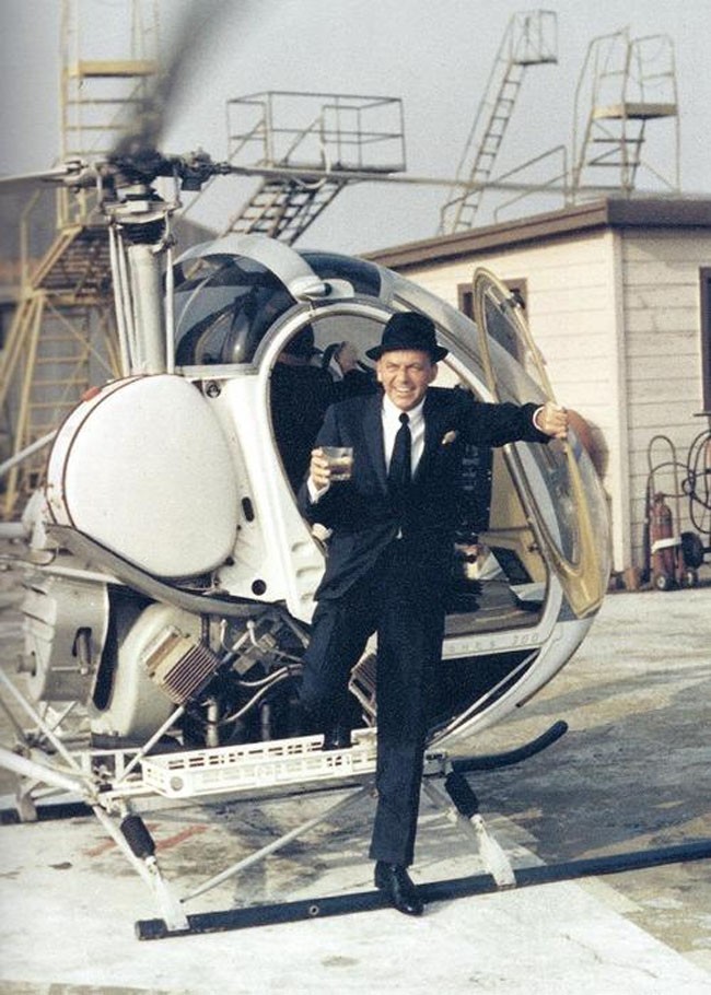 Frank Sinatra stepping out of a helicopter with a drink.