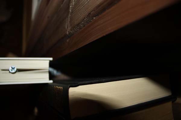 A wedge of pages was cut out, a screw attached to a piece of wood was inserted into that space. The piece of wood hidden in the book is secured to the book with glue and is also hinged to the bookcase itself.  This allows the book to move freely and in the proper way to open the latch.