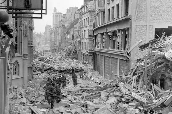 Canadian troops patrol along the destroyed Rue Saint-Pierre after removing German forces.