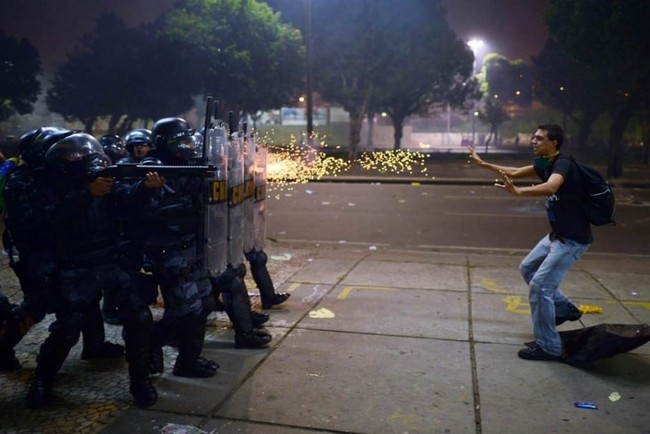 2.) Brazilian police fire on a man during protests against corruption and police brutality in 2013.