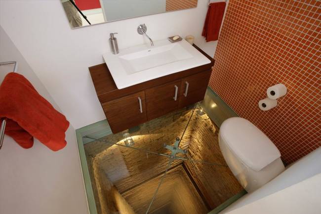 Once intended for an elevator shaft, this bathroom calls out its history using glass floors.