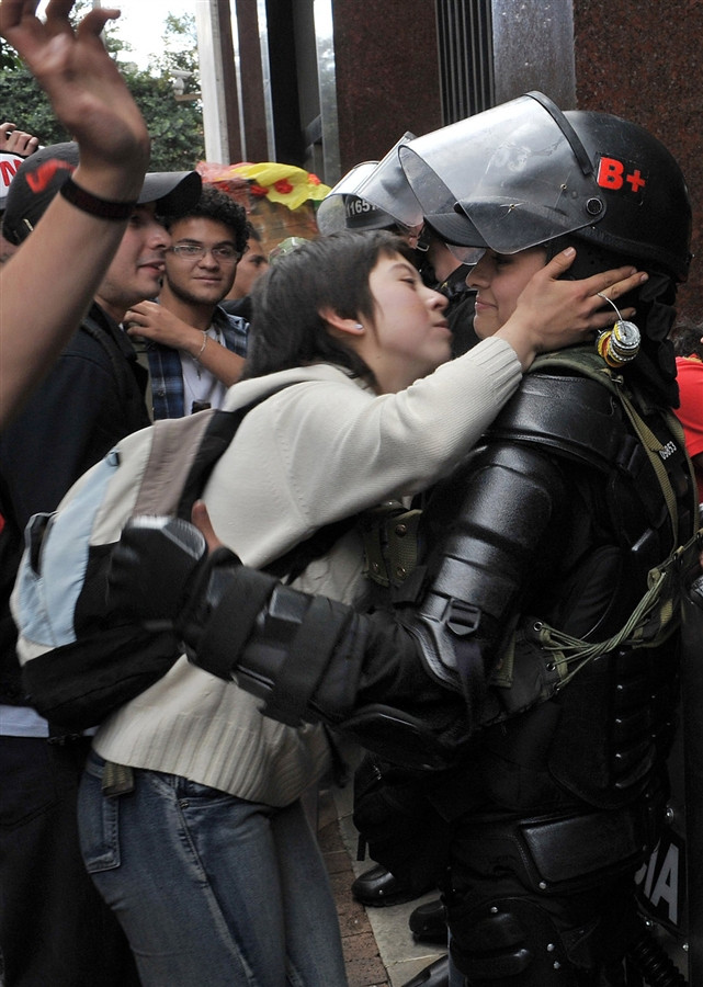 11.) A student protestor in Bogotá, Colombia tries to kiss a riot police officer.