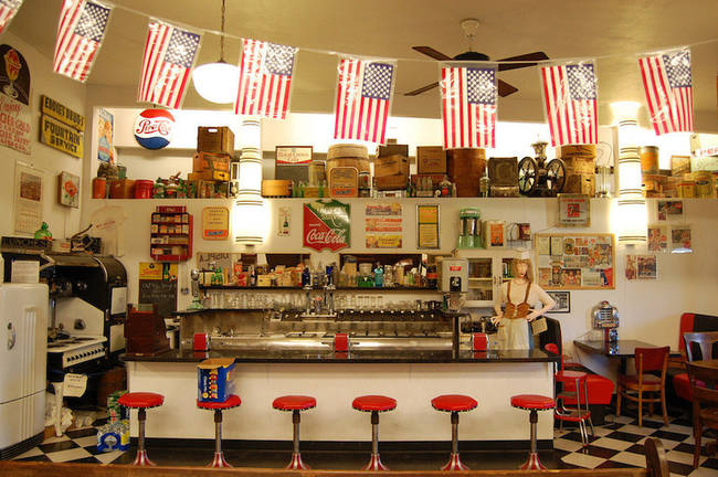 A soda shop mock-up, complete with bottles, stools and advertisements.