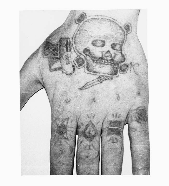 Knuckle tattoos had meanings that often told the bearer's story. The middle finger with a cross indicates this inmate was a pickpocket. The ring finger indicates that he served a complete sentence without parole. The pinky indicates that he spent a lot of time in the "punishment cell," which explains the lack of parole. The violent imagery on the back of the hand, as well as the K, signify a killer.