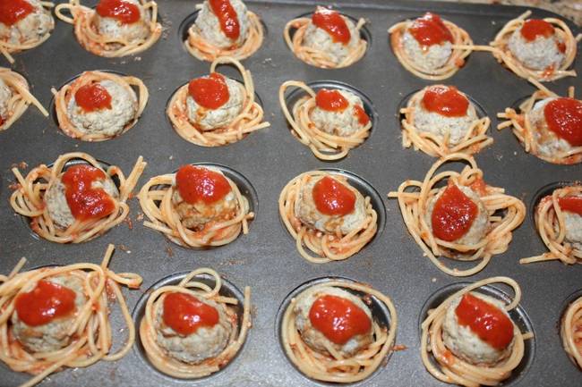 Put little nests of spaghetti into the cup-cake molds -and allow for a space where you will place your meatballs. Add a little of sauce on top as well.