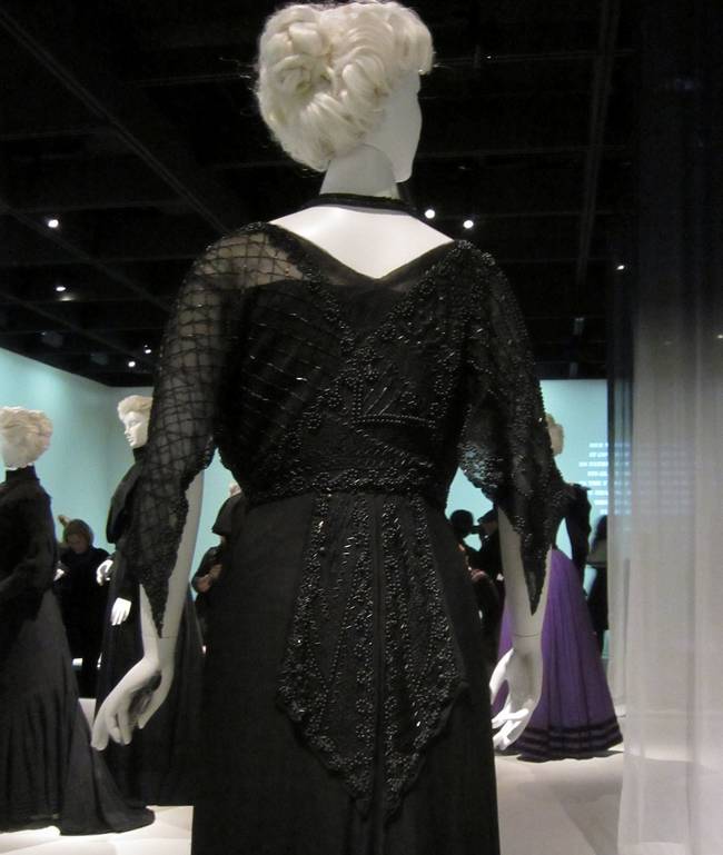 Despite the dark color, the intricate beading and sheer sleeves of this gown are definitely a fashion statement. In these days, wearing black was not for everyday use, and was not considered a "basic" color the way it is today.