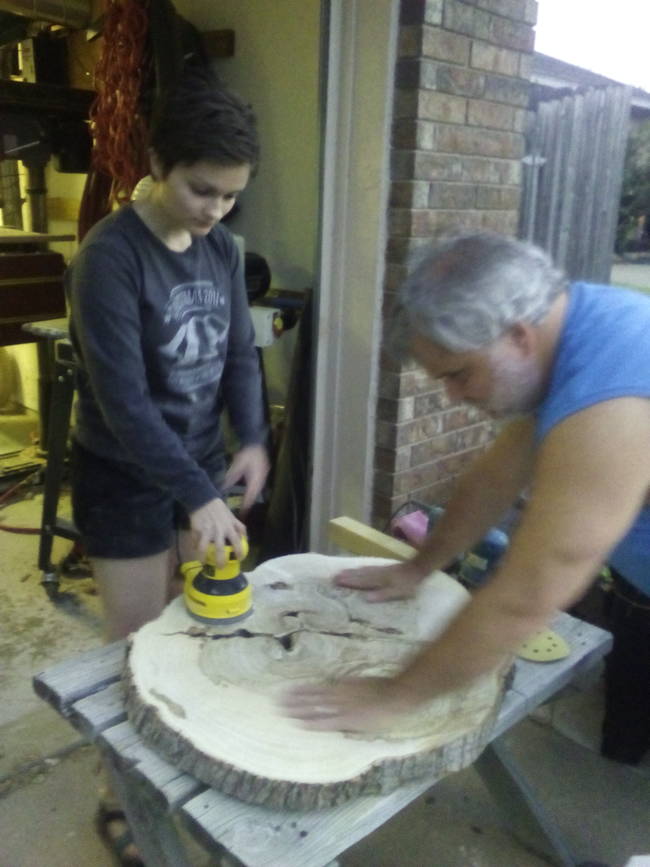 Here they are, working on sanding the piece of wood. Because he is legally blind, the father has to use his hands to measure the progress of their work.