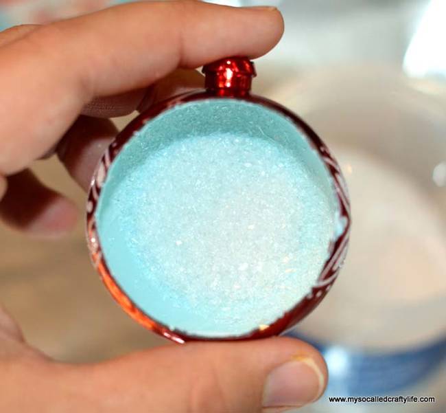 After the paint dries, paint the inside with glue and apply the glitter, but make sure to leave the bottom of the ornament clean.